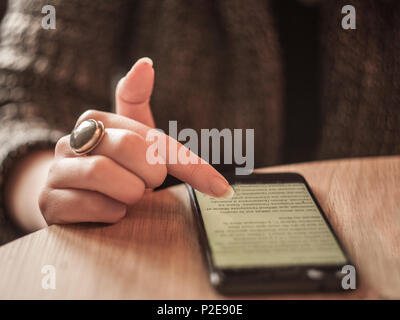 Les doigts d'une jeune femme de race blanche blanc la navigation sur un smartphone avec internet 3G afficher un écran large, plein de texte, debout sur une table Photo de Banque D'Images