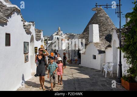 Italie, Pouilles, Alberobello, inscrite au Patrimoine Mondial de l'UNESCO, les touristes marcher dans une rue commerçante de la zona trulli bordée de trullis, ces maisons en pierre blanc chaulé, avec un toit pointu Banque D'Images