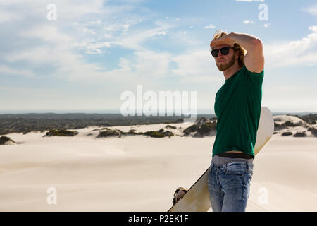 L'homme avec le sandboard debout dans le désert Banque D'Images