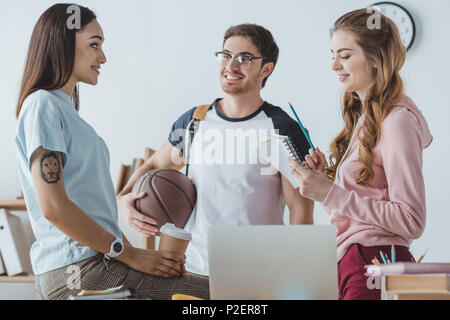 Les jeunes étudiants assis avec le basket-ball, le café d'aller et de parler ensemble copybook Banque D'Images