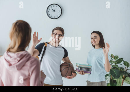 Les jeunes élèves avec des livres et de basket-ball en agitant à leur ami Banque D'Images