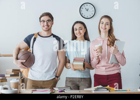 Les jeunes étudiants multiethnique holding basketball, livres, café et coffre Banque D'Images