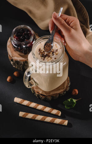 Cropped shot main de femme de mettre des copeaux de chocolat au lait frappé, menthe, sweet pailles et de Corinthe sur table Banque D'Images