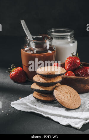 De délicieux cookies empilés avec des fraises et de bols de chocolat et de lait Banque D'Images