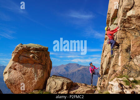 Homme d'escalade sur roche de granit rouge est belayed par femme, Mottarone, Piémont, Italie Banque D'Images