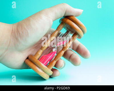 Main tenant le sablier Vintage en bois avec sable rose sur fond bleu, sable fonctionnant par les ampoules pour mesurer le temps qui passe dans une histo Banque D'Images