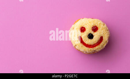 Close up télévision de laïcs heureux face smiley jaune donut isolé sur fond rose Banque D'Images