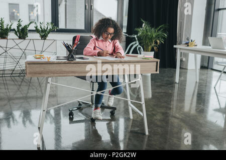 Peu d'african american girl pretending to be young et travaillant dans un bureau moderne Banque D'Images