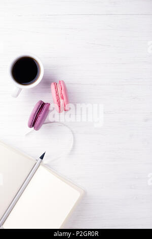 Une tasse de café, ordinateur portable deux macarons et un crayon sur la table en bois. Vue de dessus, à la verticale. Banque D'Images