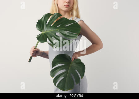 Cropped shot of young woman covering avec feuilles de monstera isolated on white Banque D'Images