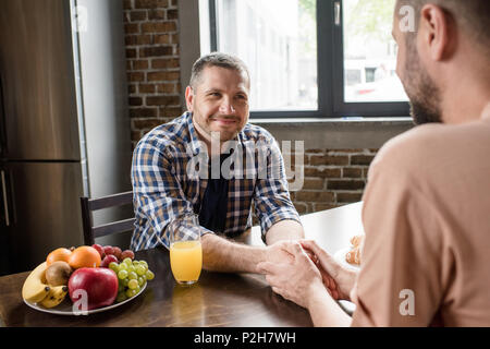 Happy gay couple holding hands at smiling les uns les autres pendant le petit-déjeuner Banque D'Images