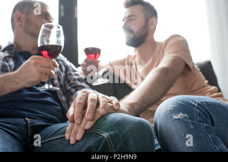 Couple homosexuel boire du vin au cours de parler alors qu'il était assis sur le canapé à la maison Banque D'Images