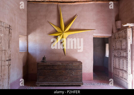 Grande étoile jaune accroché sur la paroi de la terre dans la région de hall d'entrée d'une maison berbère avec des meubles anciens en bois et de lambris de poitrine porte cloutée Banque D'Images