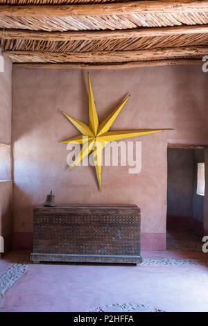 Grande étoile jaune accroché sur la paroi de la terre dans la région de hall d'entrée d'une maison berbère avec des meubles anciens en bois et de lambris de poitrine porte cloutée Banque D'Images