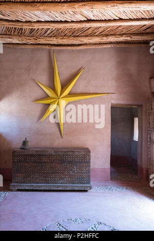 Grande étoile jaune accroché sur la paroi de la terre dans la région de hall d'entrée d'une maison berbère avec des meubles anciens en bois et de lambris de poitrine porte cloutée Banque D'Images