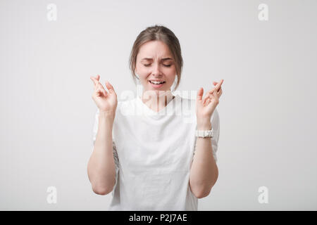 Tourné à l'intérieur de belle fille européenne en chemise blanche ayant excité regarder, gardant les doigts croisés, les yeux fermés. Elle a besoin de bonne chance avant d'aller à Banque D'Images