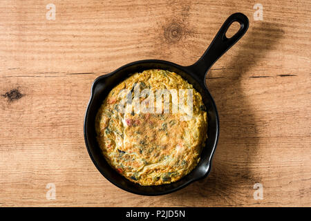Faites de la frittata des œufs et des légumes dans une poêle de fer, sur la table en bois. Vue d'en haut Banque D'Images