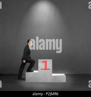 Businessman escalade sur le podium avec spot light background béton intérieurs Banque D'Images