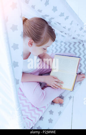 Adorable preteen girl reading fairytale en tipi Banque D'Images