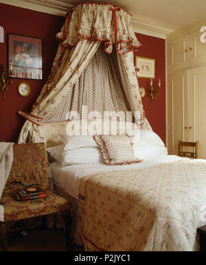 Coronet avec draperies florales au-dessus de lit avec couette floral rouge dans une chambre de style campagnard Banque D'Images