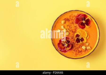 Soupe de carottes / citrouille avec le safran et fleurs comestibles pansy, vue du dessus. Banque D'Images