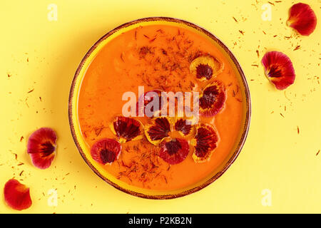 Smoothie ou soupe de carottes / citrouille avec le safran et pétales de fleur comestible, vue du dessus. Banque D'Images