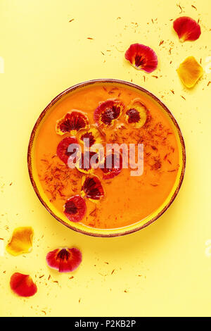 Smoothie ou soupe de carottes / citrouille avec le safran et pétales de fleur comestible, vue du dessus. Banque D'Images