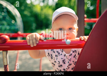 Bébé Garçon jouant dans Jeux pour enfants seulement. Portrait d'enfant à la caméra avec face au malheureux. Holding a toy sur l'aire de jeux en plein air. Banque D'Images