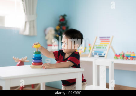 Tout-petits Asie adorable baby boy sitting on chair et en jouant avec des jouets de couleur à la maison. Banque D'Images