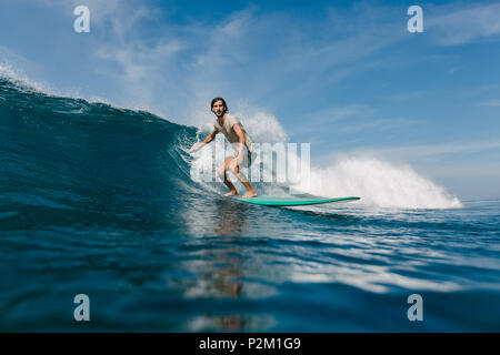 Jeune homme barbu en t-shirt mouillé équitation vagues sur une planche de surf aux beaux jours Banque D'Images