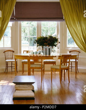 Parquet au sol dans la salle à manger avec table et chaises en bois simple en face de portes-fenêtres avec stores et rideaux verts mauve Banque D'Images