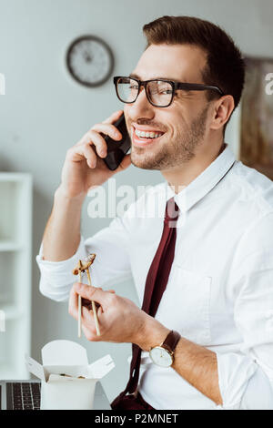 Classy businessman eating chinese food while talking on smartphone Banque D'Images