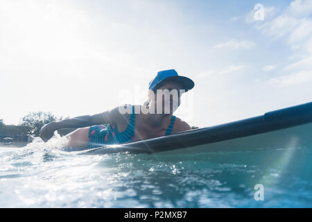 Jolie femme souriante en cap allongé sur le surf de l'océan en conseil Banque D'Images