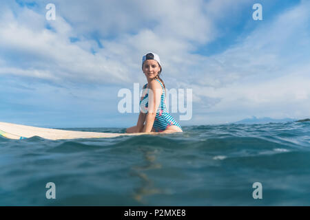 Vue de côté de femme en costume de bain assis sur une planche de surf dans la région de ocean Banque D'Images