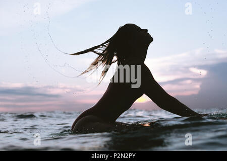 Silhouette de femme cheveux fouetter tout en vous reposant sur le surf de l'océan en conseil sur le coucher du soleil Banque D'Images