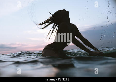 Silhouette de femme cheveux fouetter tout en vous reposant sur le surf de l'océan en conseil sur le coucher du soleil Banque D'Images