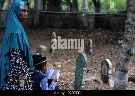 Un enfant vu lire le Coran à côté d'une tombe avec sa mère au cours du pèlerinage. Les musulmans vu de leurs proches tombe, lors d'un pèlerinage au cimetière public à Lhokseumawe Ville. La plupart des musulmans à Aceh déjà fait le dernier pèlerinage grave avant d'entrer dans le mois sacré du Ramadan et le jour de l'Aïd al-Fitr, à prier pour les familles de ceux qui sont morts. Banque D'Images