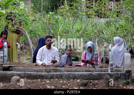 Une femme vu lire le Coran à côté d'une tombe au cours du pèlerinage. Les musulmans vu de leurs proches tombe, lors d'un pèlerinage au cimetière public à Lhokseumawe Ville. La plupart des musulmans à Aceh déjà fait le dernier pèlerinage grave avant d'entrer dans le mois sacré du Ramadan et le jour de l'Aïd al-Fitr, à prier pour les familles de ceux qui sont morts. Banque D'Images