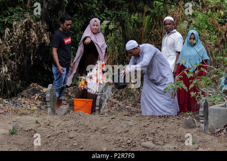 Un musulman avec sa famille vu l'abandon de l'eau sur un des parents tombe au cours du pèlerinage. Les musulmans vu de leurs proches tombe, lors d'un pèlerinage au cimetière public à Lhokseumawe Ville. La plupart des musulmans à Aceh déjà fait le dernier pèlerinage grave avant d'entrer dans le mois sacré du Ramadan et le jour de l'Aïd al-Fitr, à prier pour les familles de ceux qui sont morts. Banque D'Images