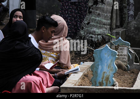 Lhokseumawe, Indonésie. 16 Juin, 2018. Un homme vu lire le Coran à côté d'une tombe au cours du pèlerinage.musulmans vu de leurs proches tombe, lors d'un pèlerinage au cimetière public à Lhokseumawe Ville. La plupart des musulmans à Aceh déjà fait le dernier pèlerinage grave avant d'entrer dans le mois sacré du Ramadan et le jour de l'Aïd al-Fitr, à prier pour les familles de ceux qui sont morts. Credit : Maskur a/SOPA Images/ZUMA/Alamy Fil Live News Banque D'Images