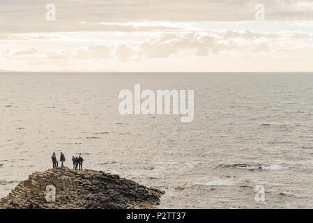 Les gens debout sur les rochers à côté de l'océan à la Chaussée des Géants en Irlande du Nord. Banque D'Images