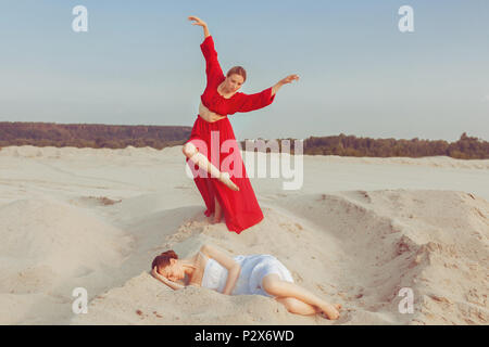 Jeune femme couchée sur le sable, l'autre femme dans une robe rouge danser à côté d'elle. Banque D'Images