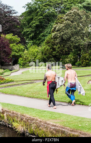 Deux surfers carrying surfboards leur marche à travers un jardin paysager à Newquay en Cornouailles. Banque D'Images
