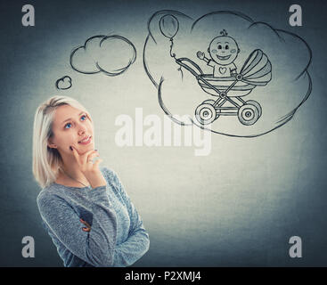 Portrait of smiling woman looking up et d'imaginer un bébé dans sa poussette. Rêve d'un enfant avec un visage positif expression, isolé sur wa gris Banque D'Images