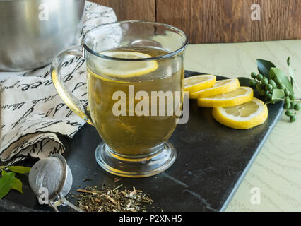 Feuilles en vrac Thé Vert - chaud dans une tasse en verre clair avec une tranche de citron flottant sur le haut de la boisson. Bol de thé séchées, citrons, et organisé Banque D'Images