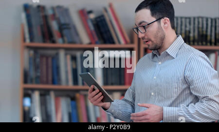 Les jeunes mâles des visioconférences en comprimé à bibliothèque Banque D'Images