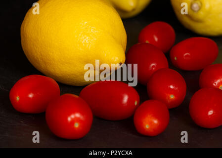Les citrons jaunes et rouges tomates bébé isolé sur un fond sombre sur une surface en ardoise. Concept de saine alimentation Fruits Banque D'Images