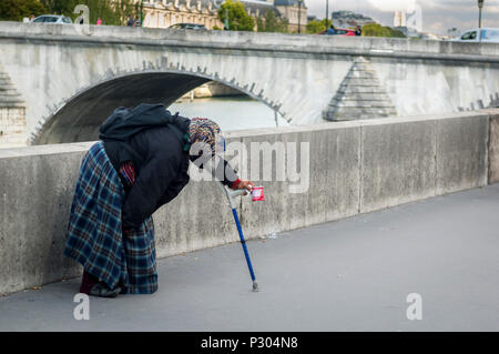 Une vieille femme sans-abri, s'appuyant sur un bâton de marche de soutien, près d'un pont sur la Seine à Paris, à la mendicité pour l'argent. Banque D'Images