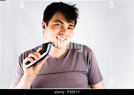 Un jeune homme de son menton d'un rasoir électrique. Adolescent tenant sa tondeuse électrique. Beau jeune homme est à l'aide d'un rasoir électrique et lookin Banque D'Images