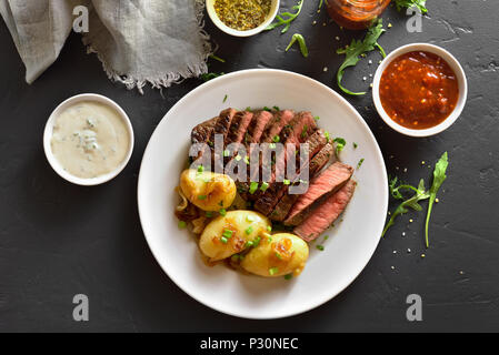 Steak juteux à point le boeuf avec pommes de terre au four sur plaque blanche sur fond noir table de pierre. Haut de la vue, télévision lay Banque D'Images